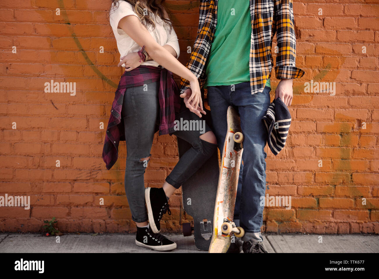 La section basse du couple holding hands while standing against brick wall Banque D'Images