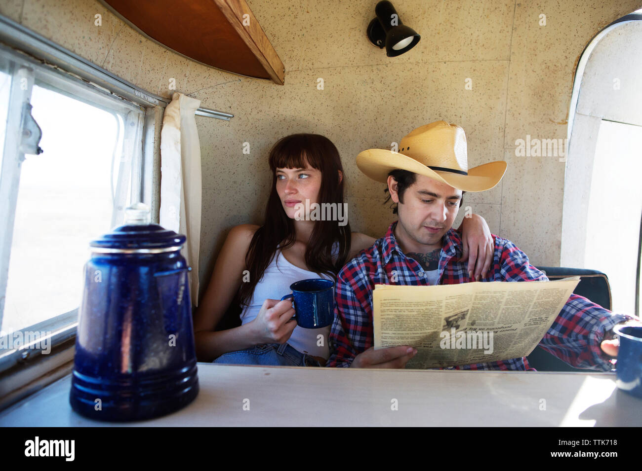 Man reading newspaper tout en regardant par la fenêtre de la femme dans le camping-car Banque D'Images Man reading newspaper tout en regardant par la fenêtre de la femme dans le camping-car Banque D'Images