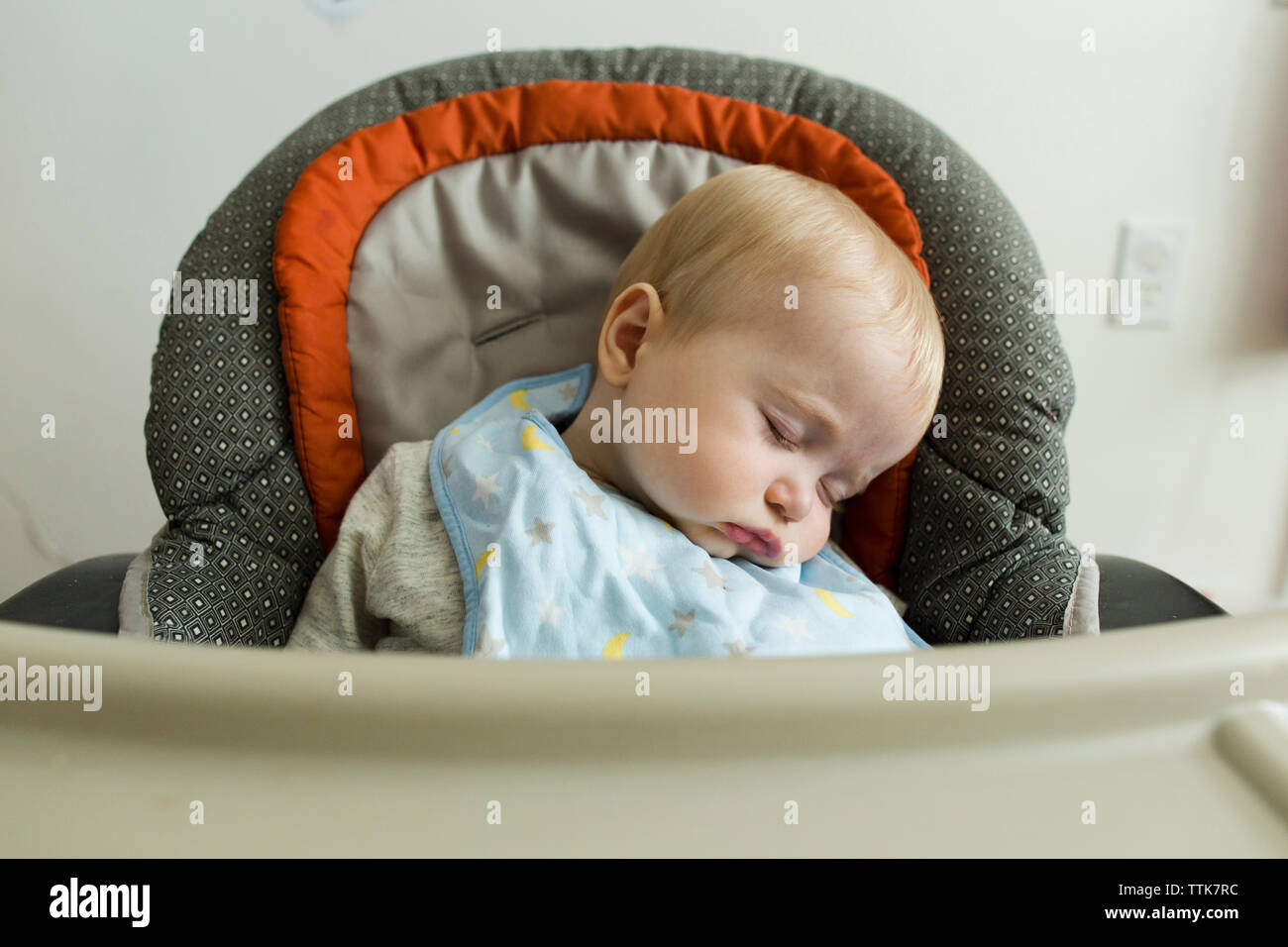 Mignon bébé garçon endormi sur la chaise haute à la maison Banque D'Images