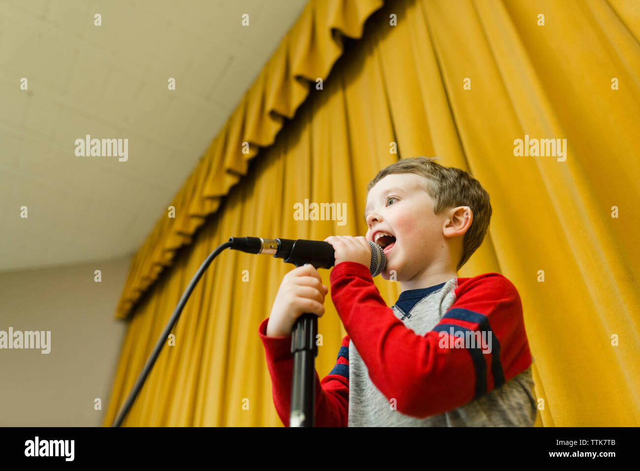 Garçon chanter sur scène au micro contre rideaux jaunes Banque D'Images