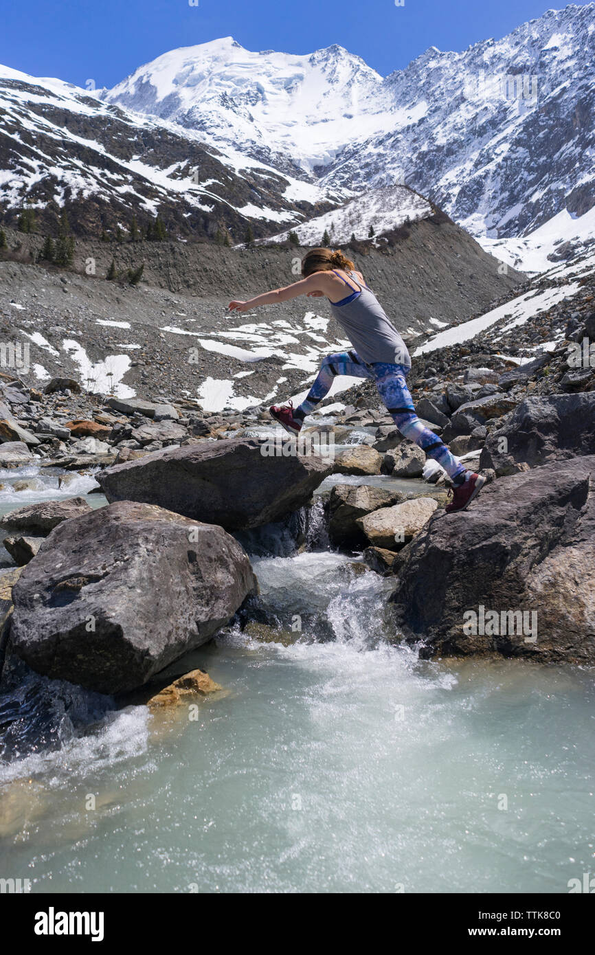 Vue de côté femme sautant sur les roches par contre, montagnes aux sommets enneigés Banque D'Images