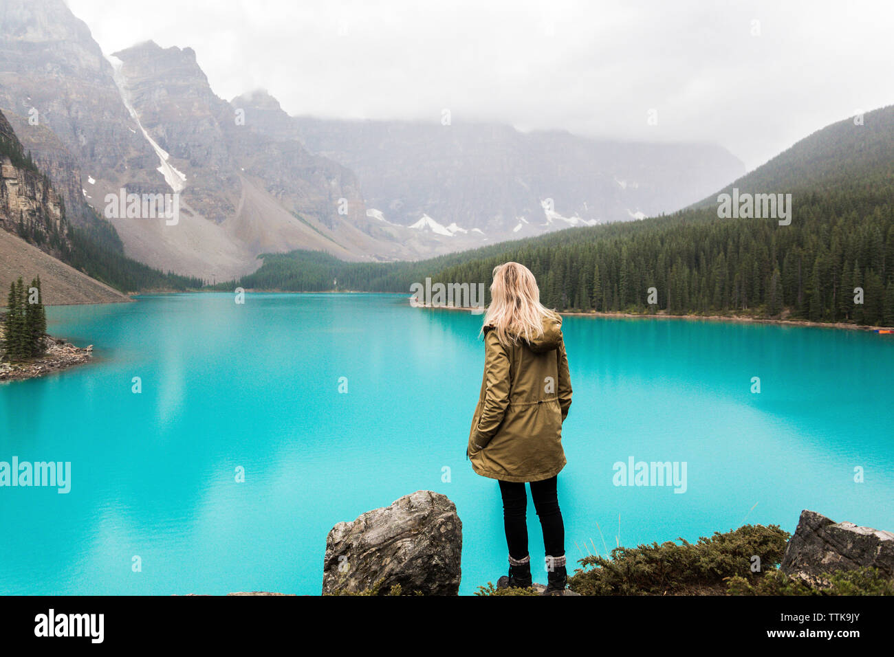 Vue arrière du female hiker with hand in pocket debout près du lac Moraine contre la montagne au parc National Banff Banque D'Images