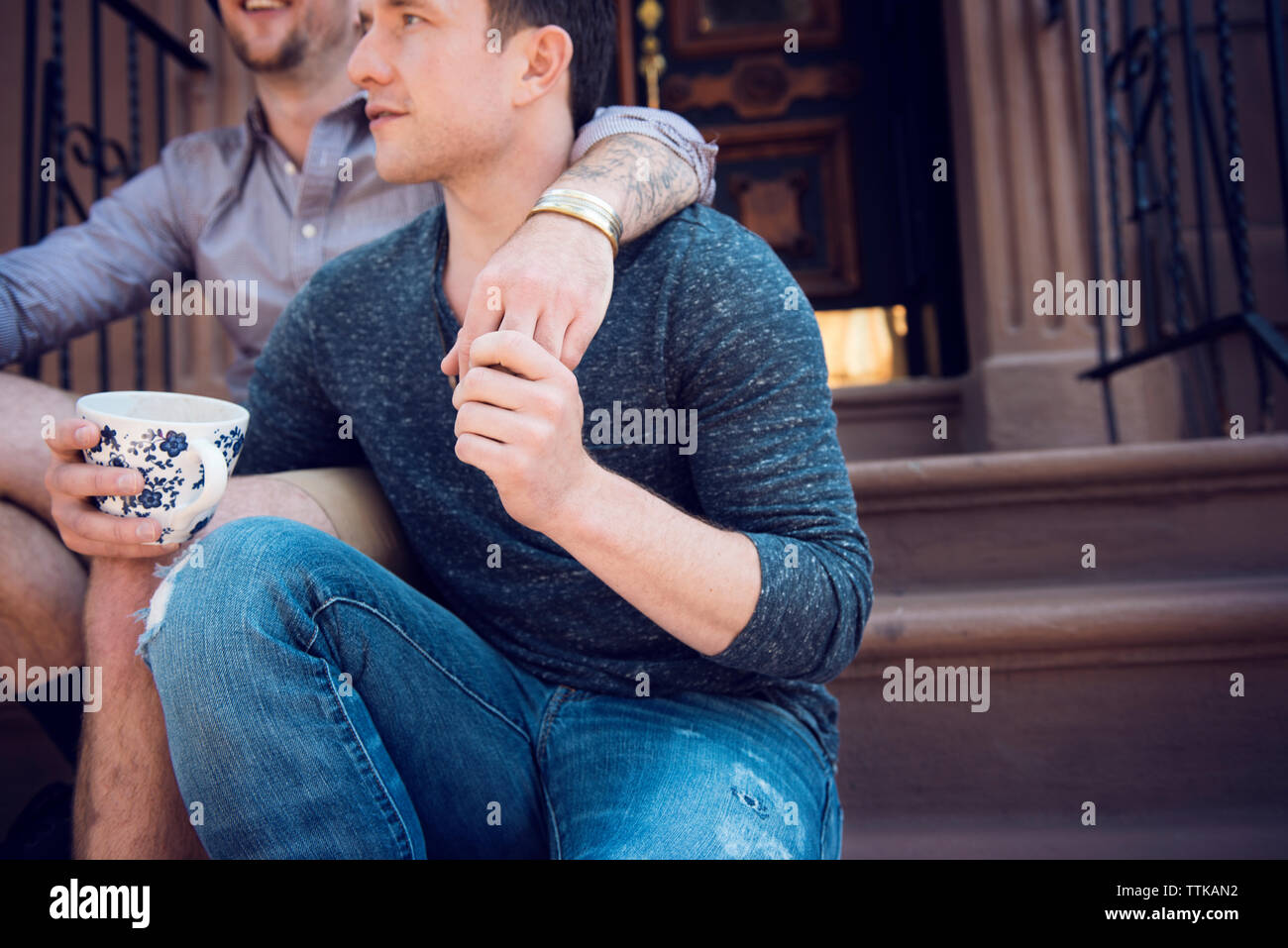 Portrait gay couple sitting on steps outside house Banque D'Images