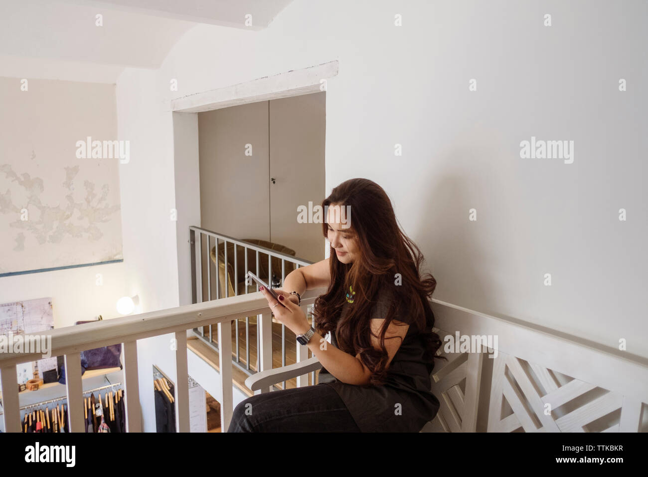 Woman using tablet computer while sitting by railing Banque D'Images