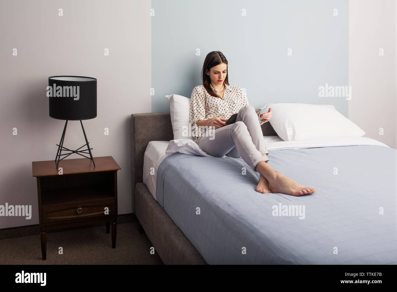 Businesswoman reading magazine alors que sitting on bed in hotel room Banque D'Images