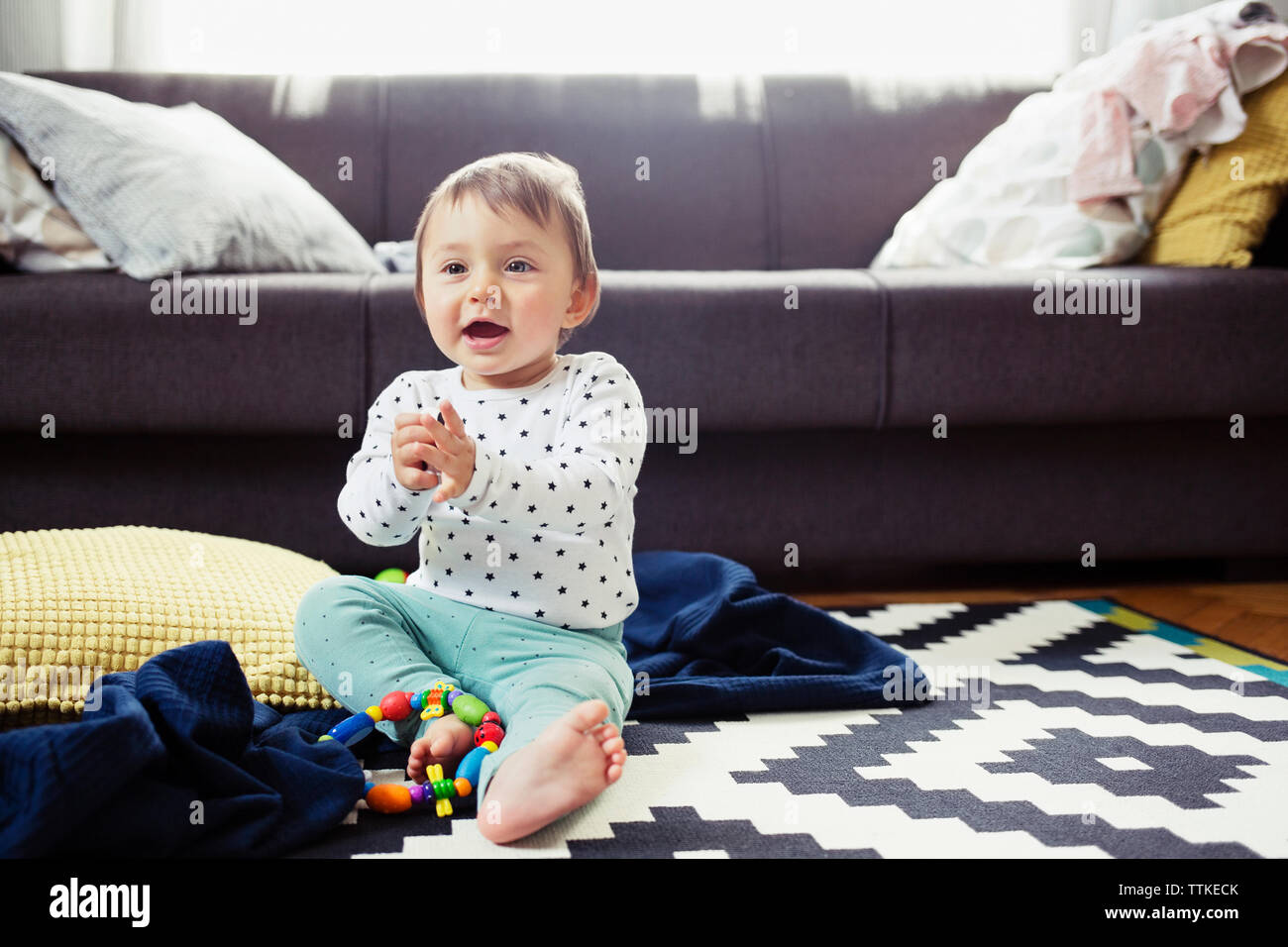 Happy baby girl sitting on rug in living room Banque D'Images