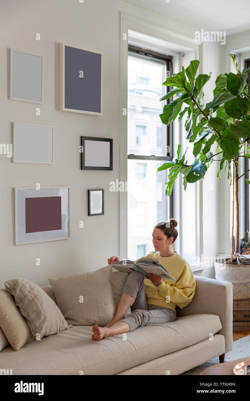 Woman Reading magazine tout en vous relaxant sur le canapé à la maison Banque D'Images