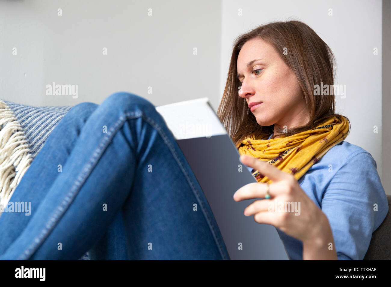 Woman Reading magazine, assis sur un canapé à la maison Banque D'Images