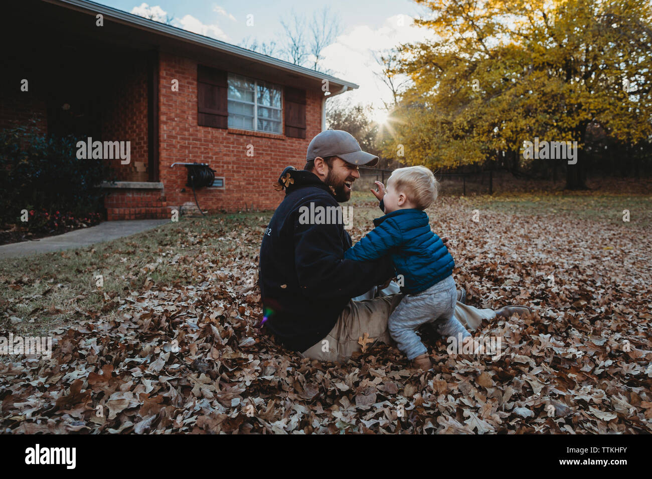 Heureux père jouant avec son fils alors qu'il était assis sur les feuilles d'automne at yard Banque D'Images