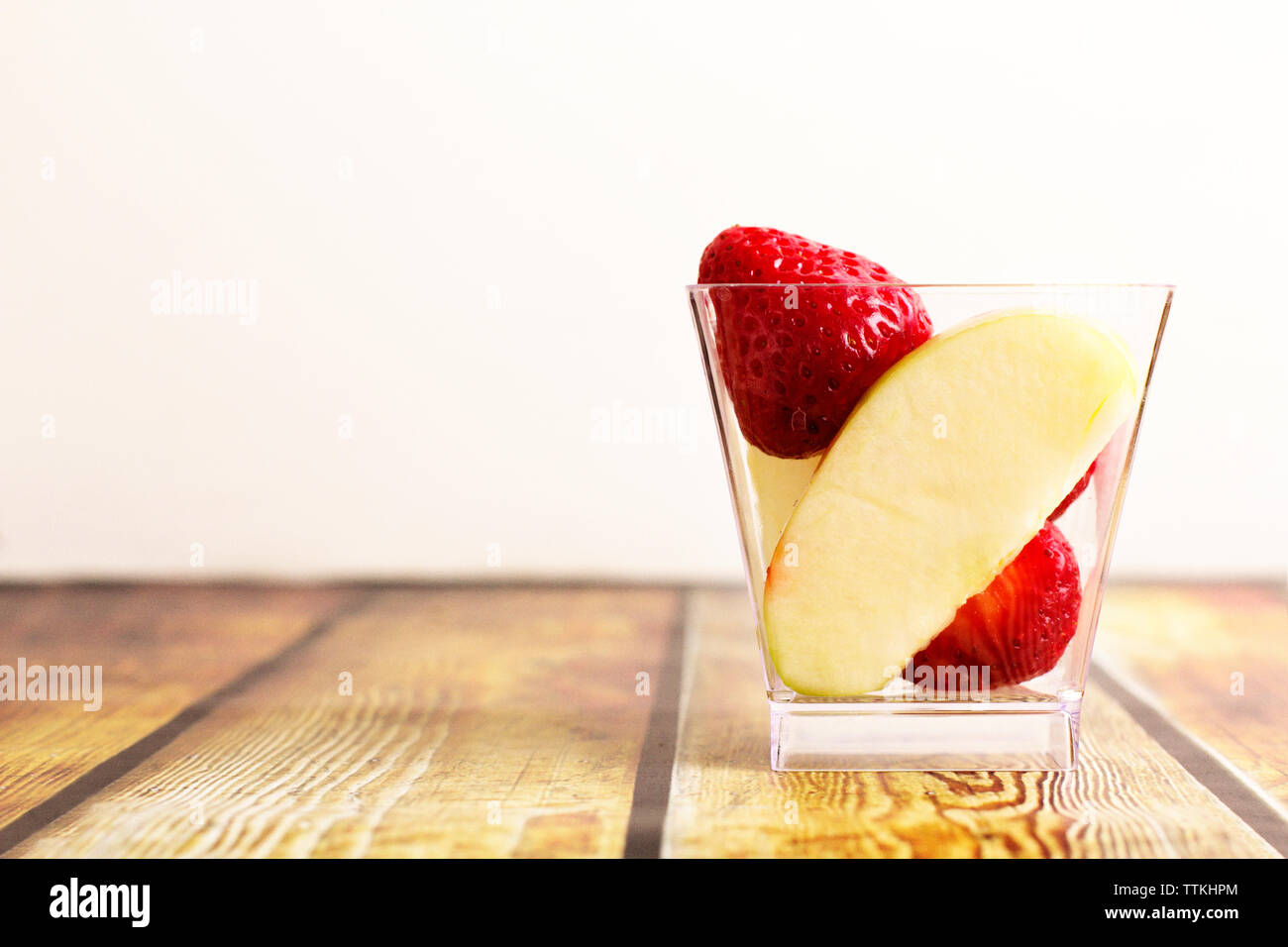 Close-up de fraises et la tranche de pomme dans le récipient sur la table contre fond blanc Banque D'Images