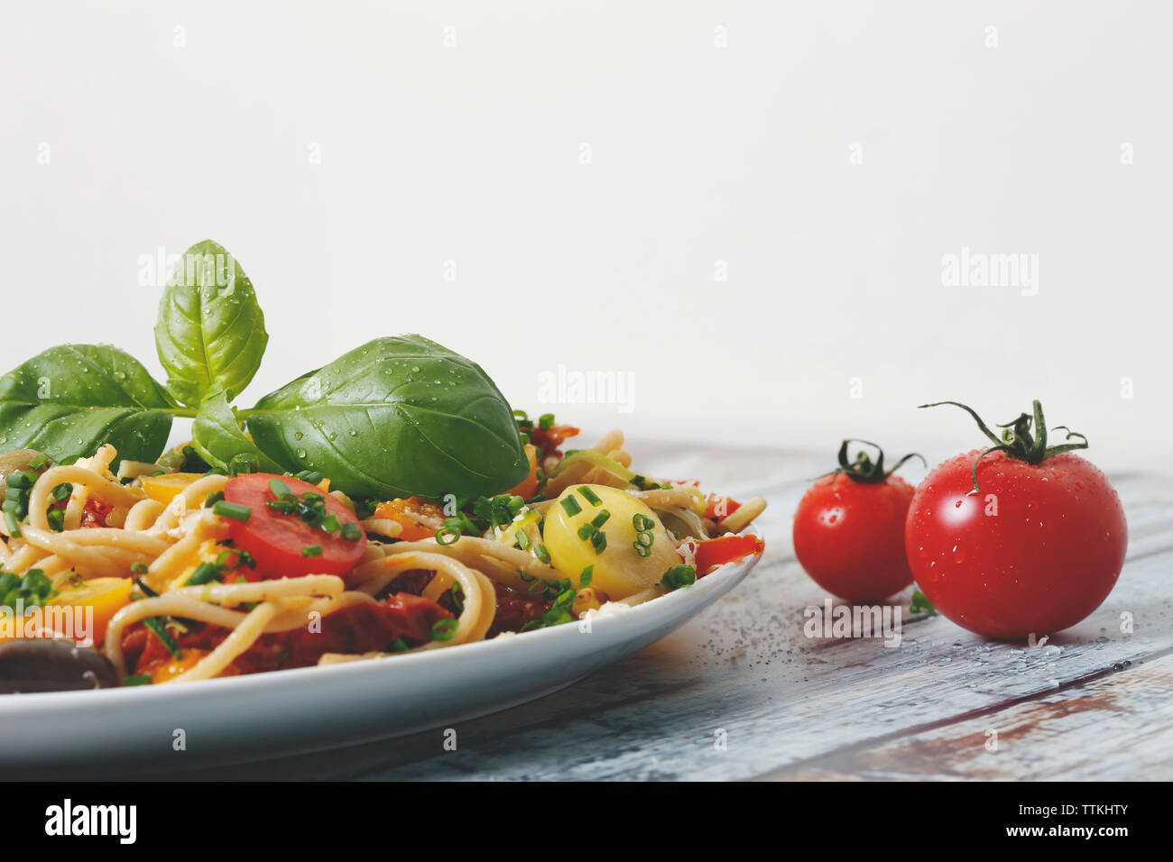 Close-up de nouilles servies dans la plaque par tomates sur table en bois contre fond blanc Banque D'Images