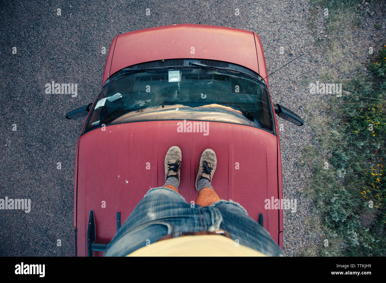 La section basse de l'homme debout sur le toit de voiture rouge Banque D'Images