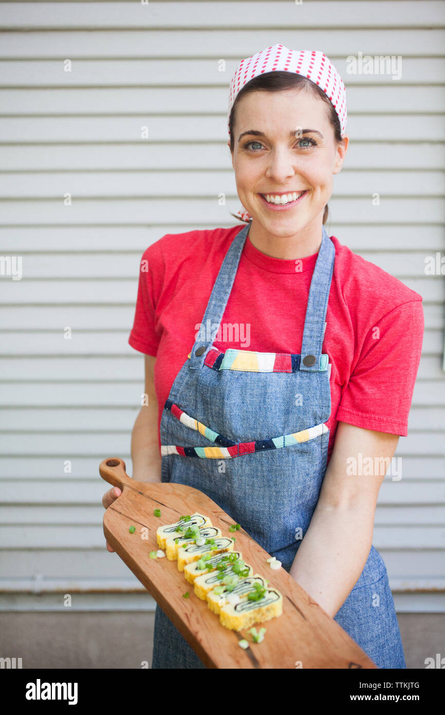 Portrait of smiling chef holding food sur le service à bord tout en se tenant dans une cuisine commerciale Banque D'Images