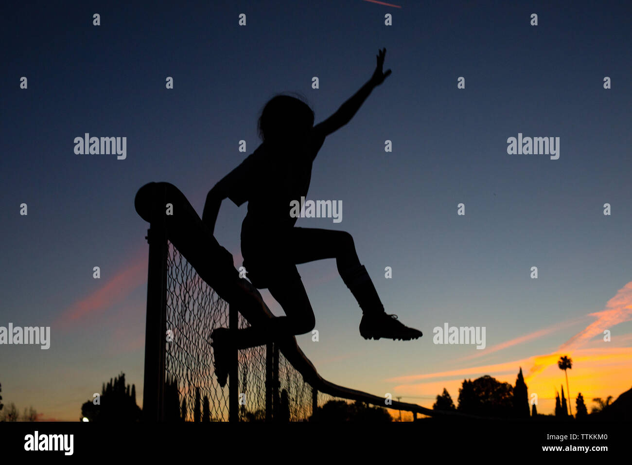 Silhouette fille sportive jumping over fence immuniser contre le ciel Banque D'Images