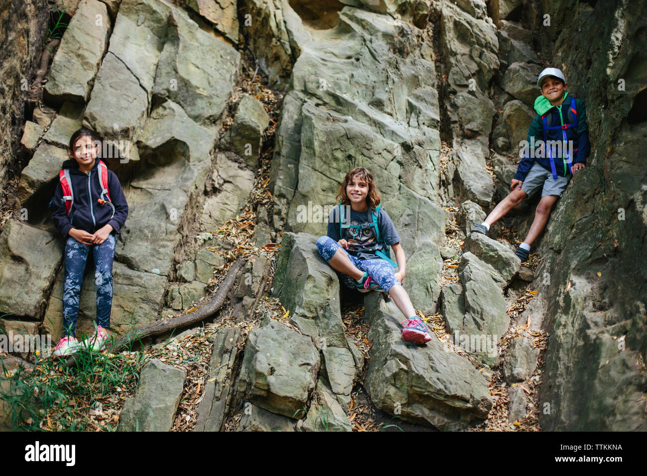 Low angle portrait of happy siblings climbing on rocks Banque D'Images