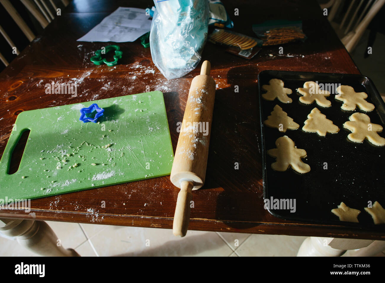 Vue à angle élevé des biscuits de noël dans la plaque de cuisson avec rouleau à pâtisserie et planche à découper sur la table en bois à la maison Banque D'Images