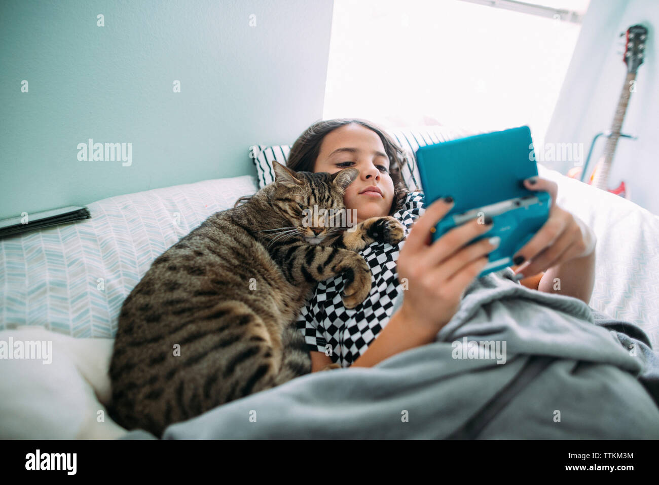 High angle view of girl playing video game en position couchée avec cat on bed at home Banque D'Images