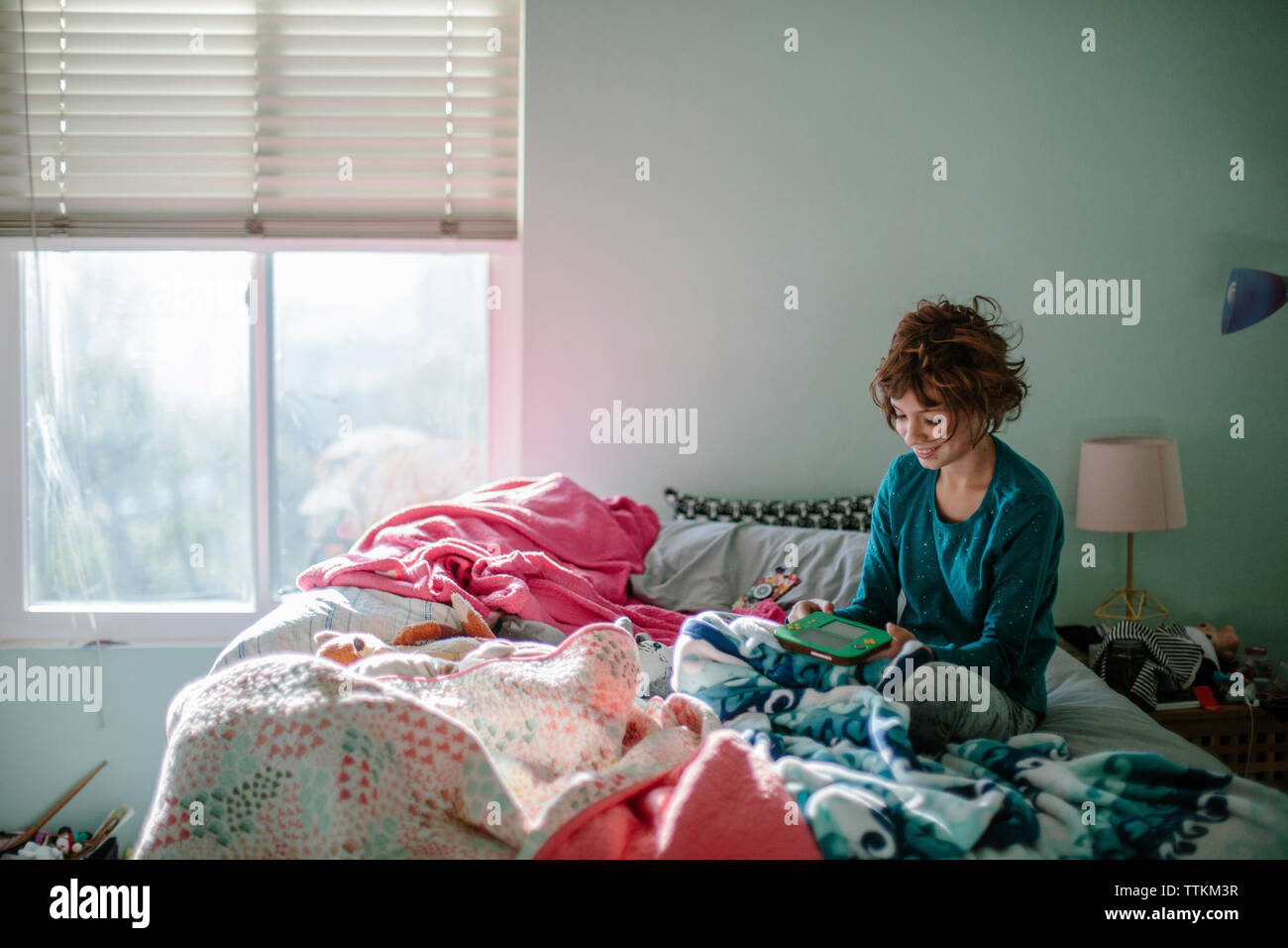 Smiling girl playing video game while sitting on bed at home Banque D'Images