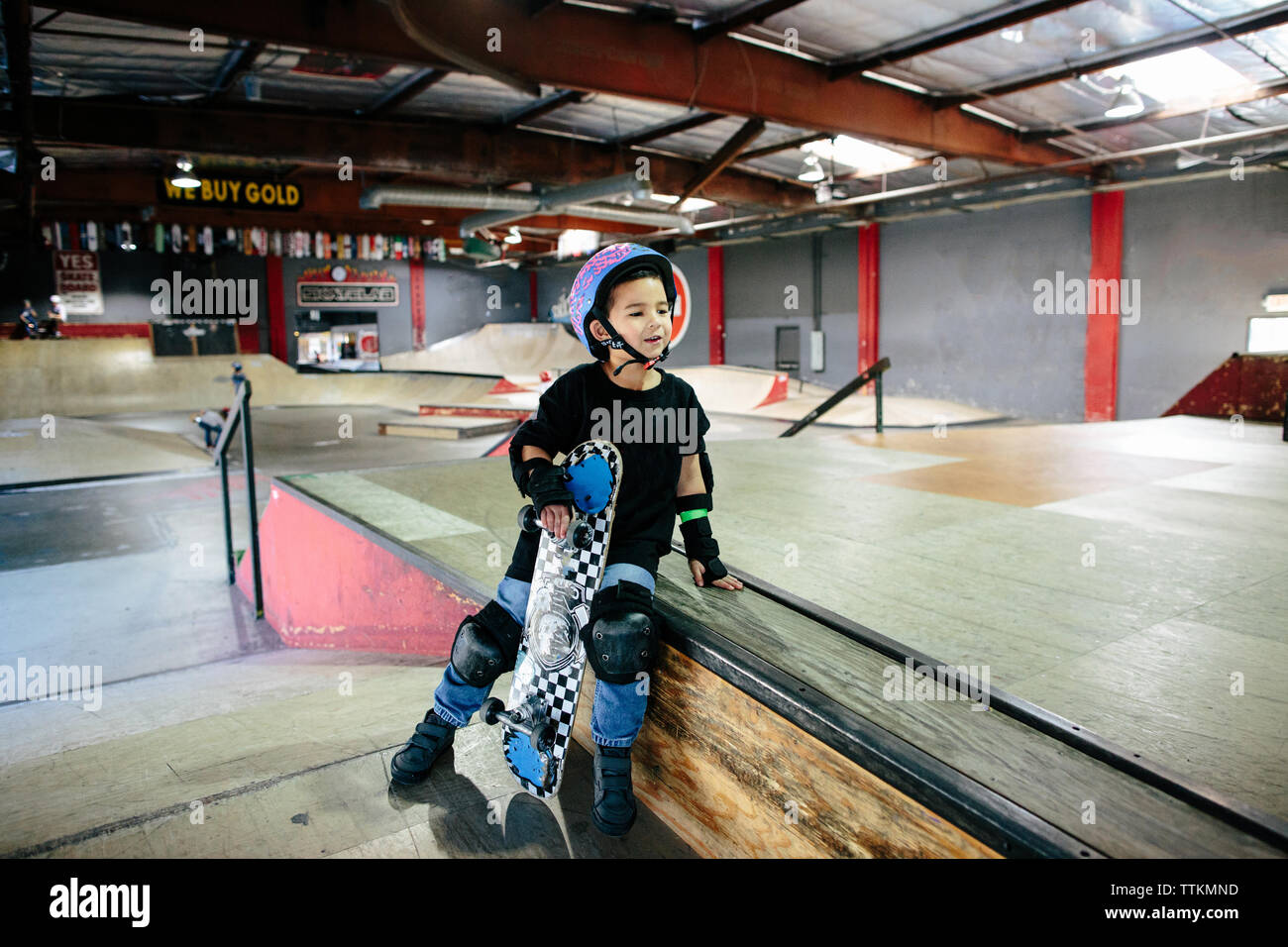 Petit garçon est assis en maintenant son skateboard au skatepark Banque D'Images