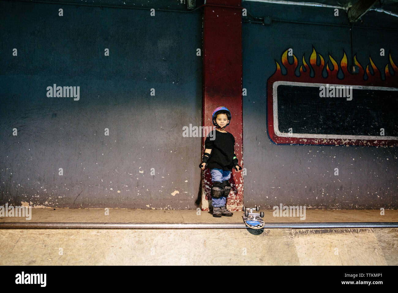 Petit garçon se dresse sur le sommet d'une rampe de skate à côté de skateboard Banque D'Images