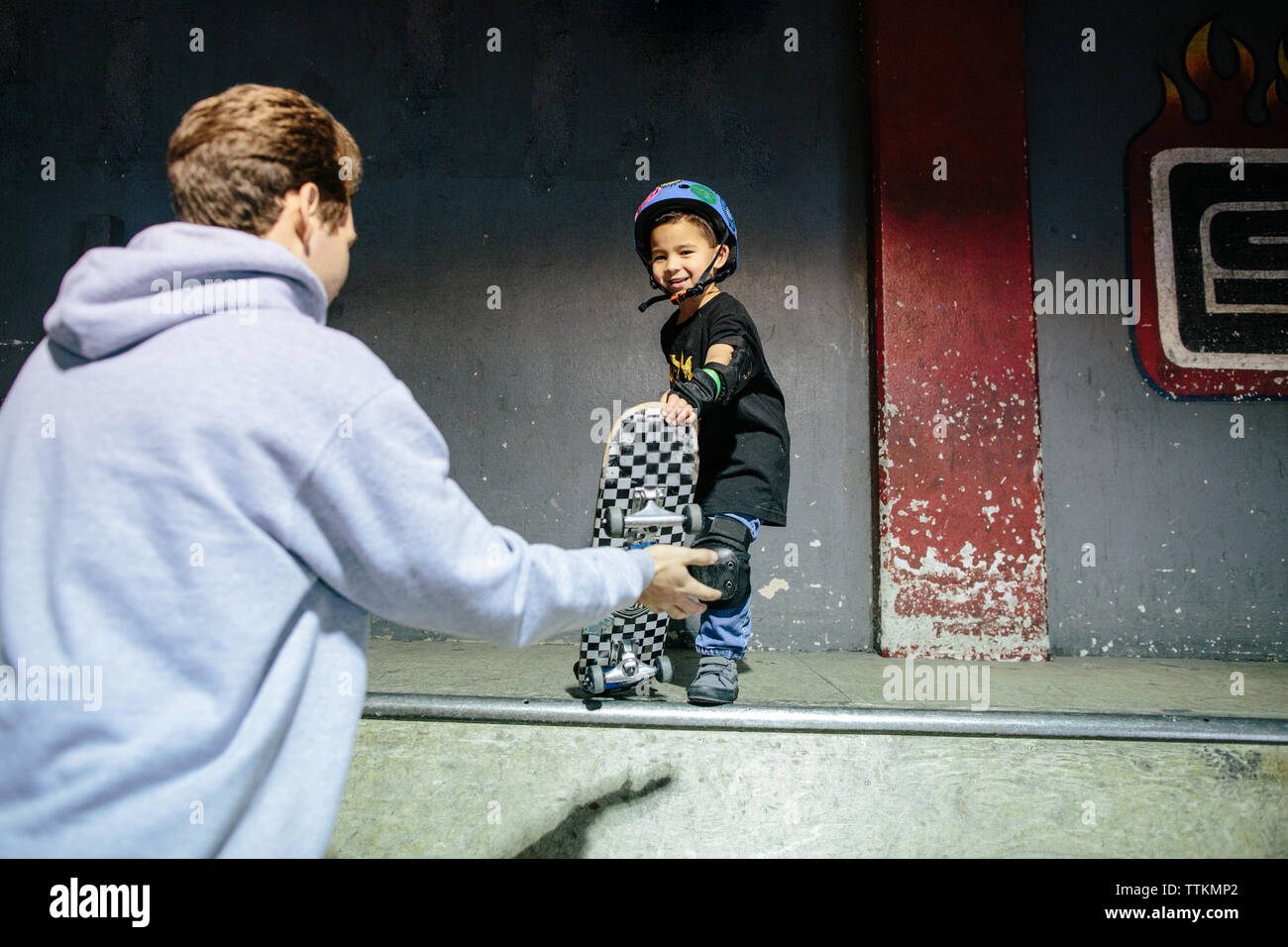 Petit garçon preps son skateboard pour descendre une rampe avec moniteur Banque D'Images