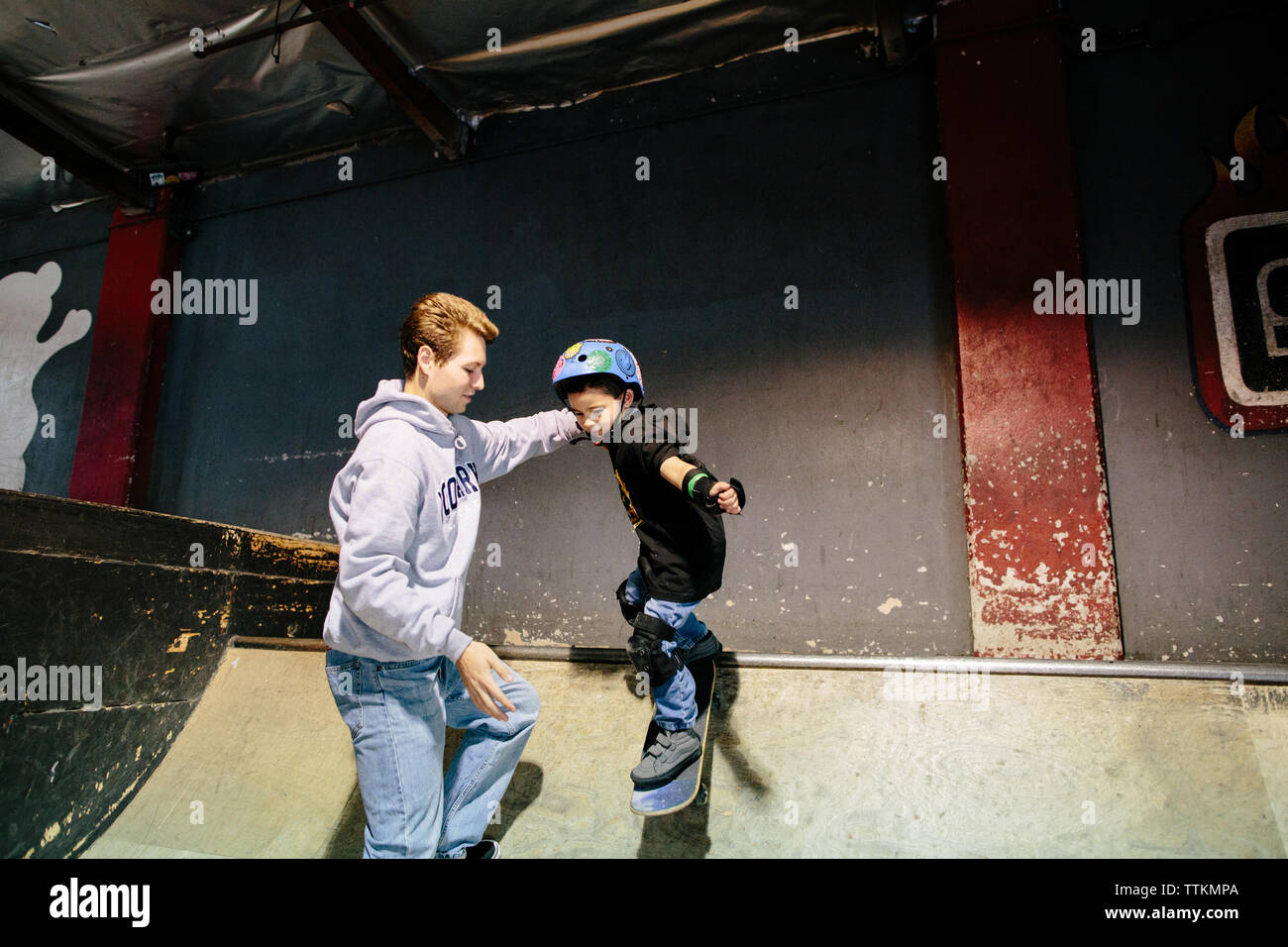 Petit garçon descend une rampe de skate alors que détient l'instructeur sur Banque D'Images