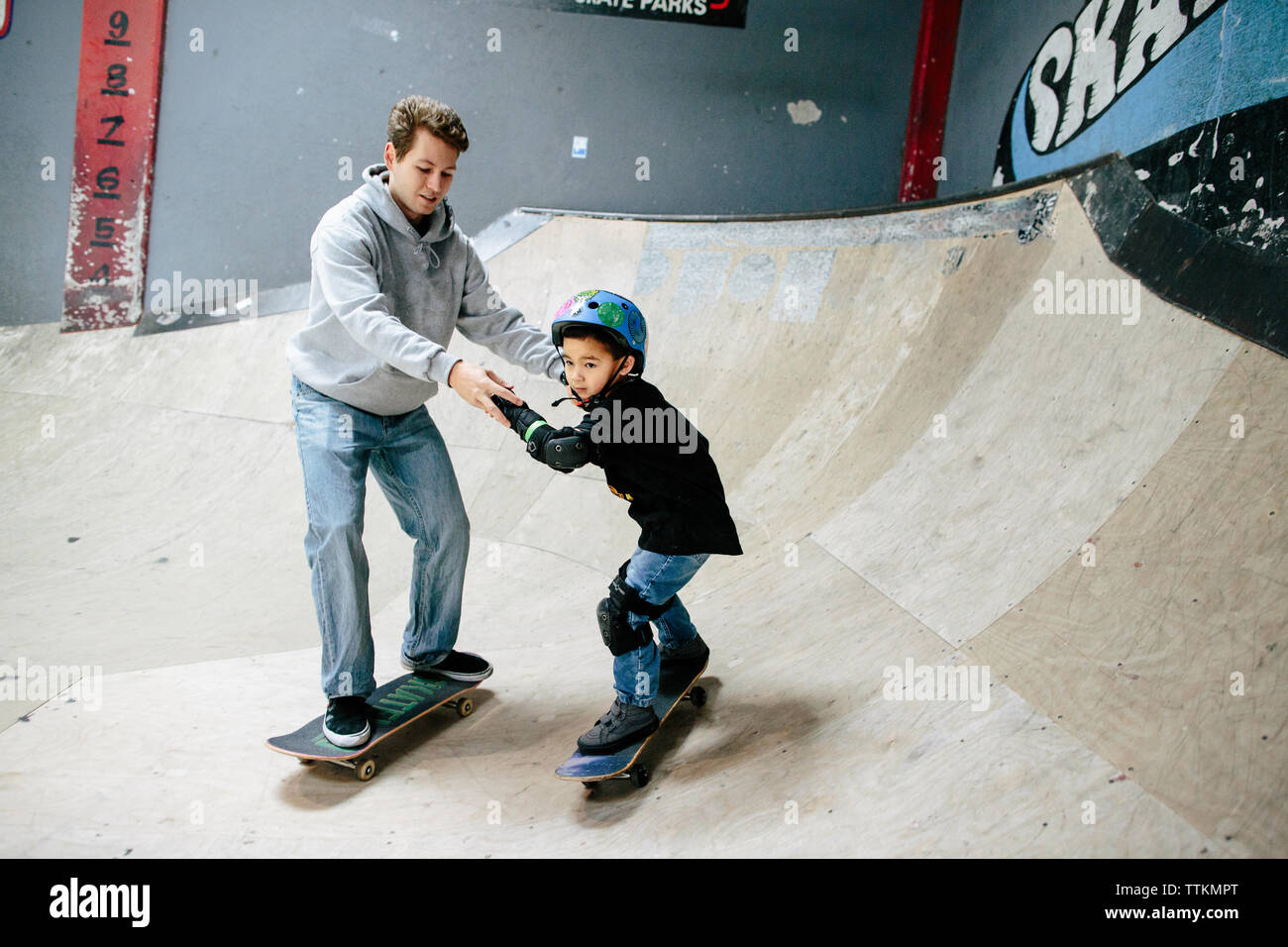Petit garçon tient la main de skateboard skateboard tandis que l'instructeur Banque D'Images
