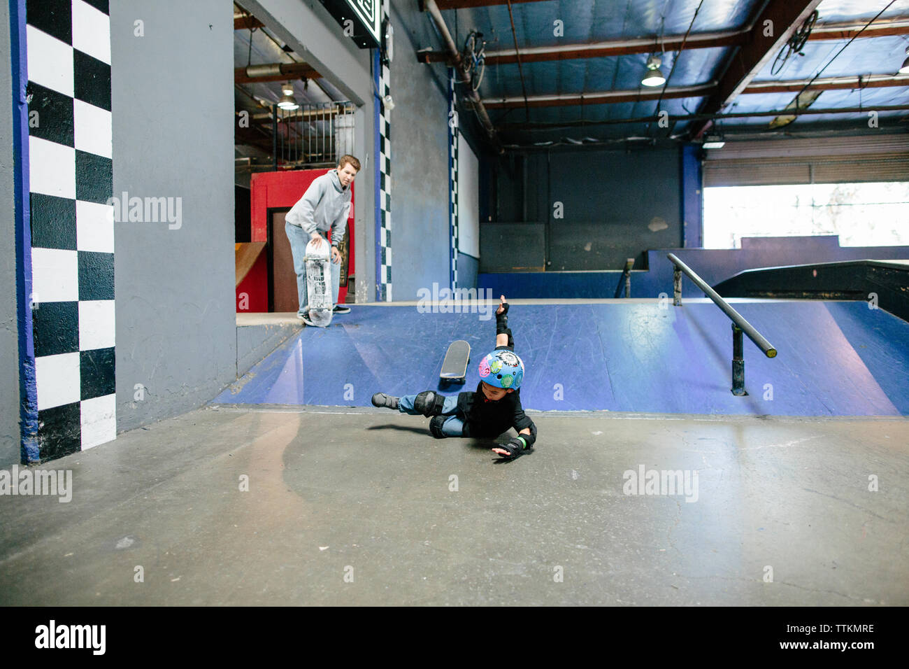 Petit garçon tombe de skateboard tandis que les montres de l'instructeur Banque D'Images