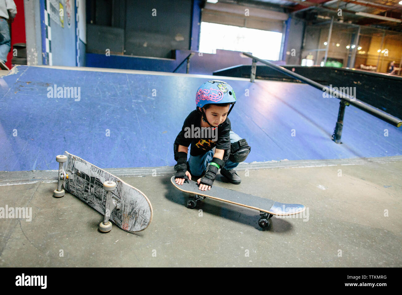 Petit garçon s'accroupit vers le bas pour mettre en place son skateboard Banque D'Images