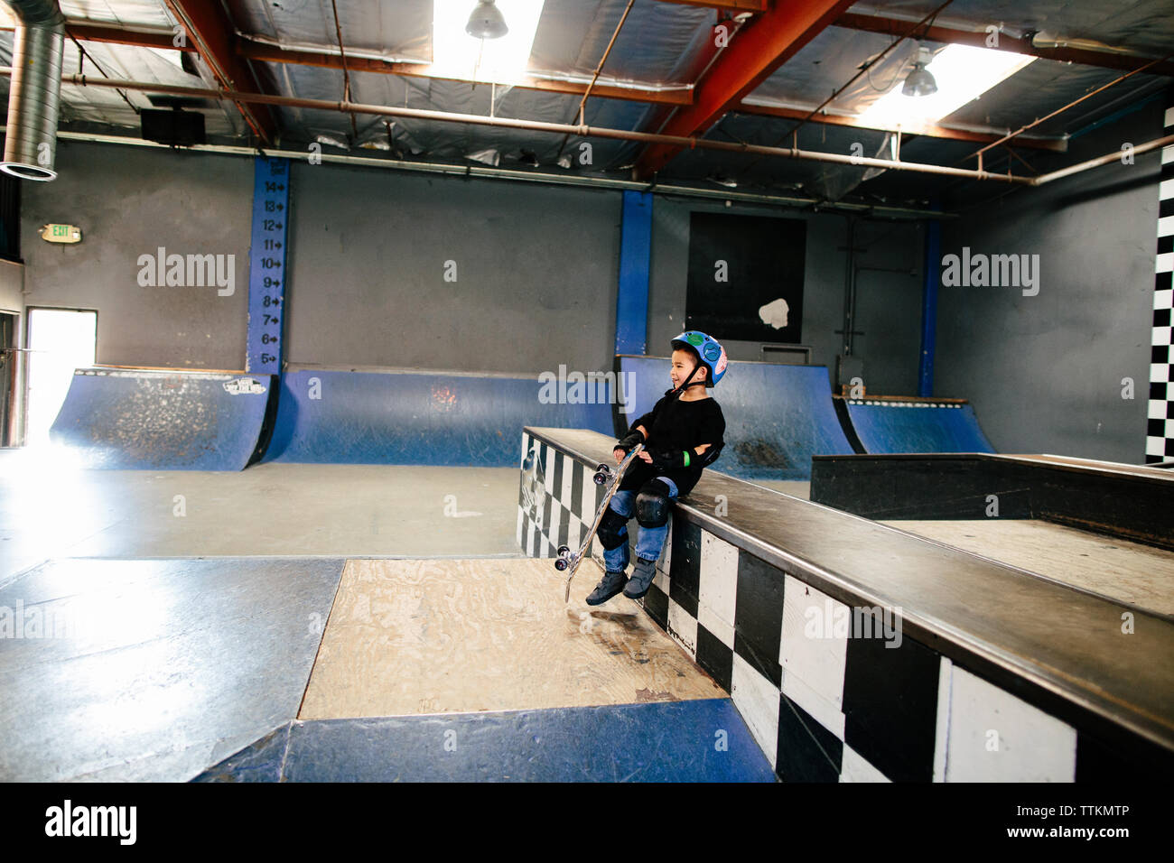 Petit garçon s'assied tout en maintenant son skateboard en skatepark Banque D'Images