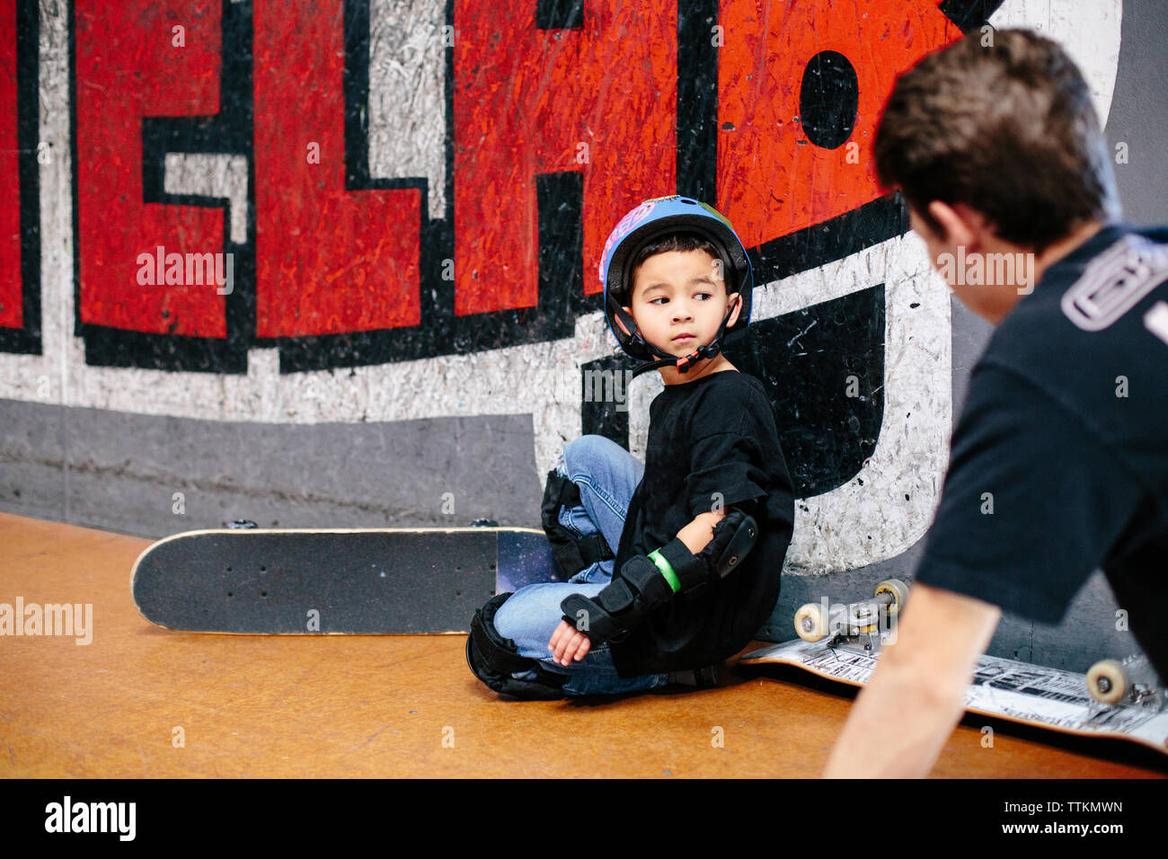 Petit garçon à genoux à côté de son skateboard à enseignant passé Banque D'Images