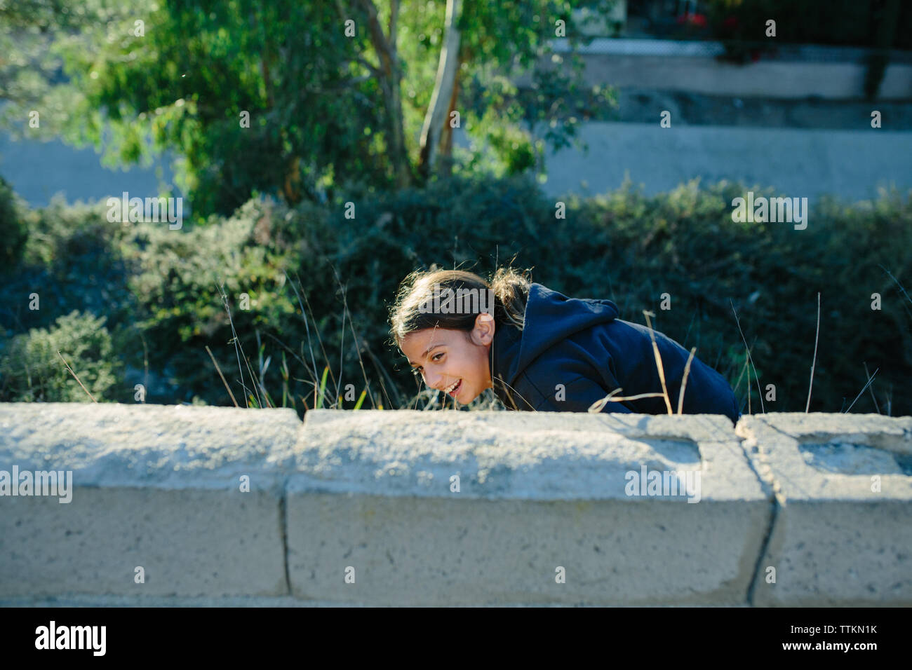 Girl se penche de manière ludique à essayer de se cacher derrière le mur Banque D'Images