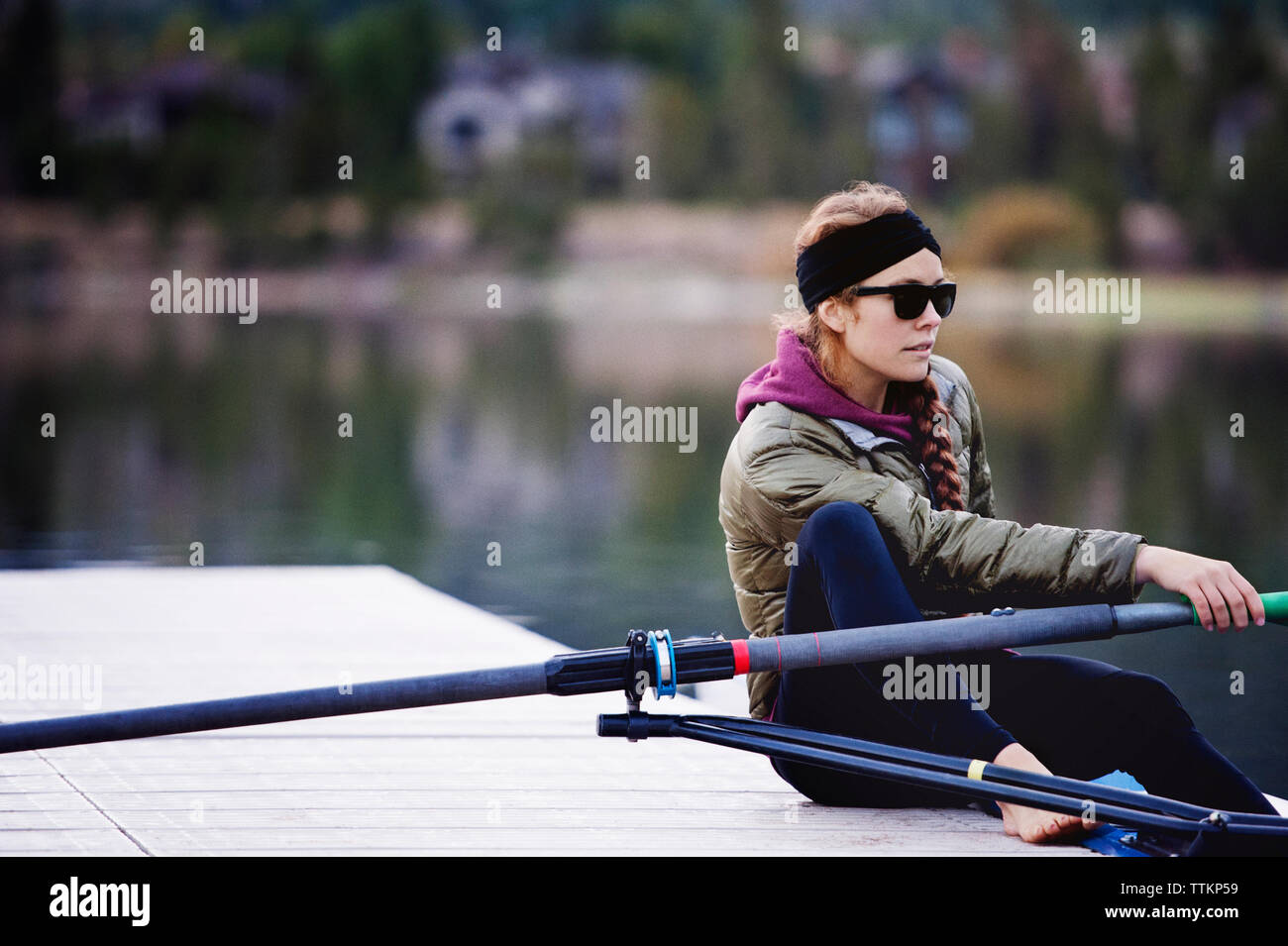 Young woman sitting on jetty avec oar par lake Banque D'Images