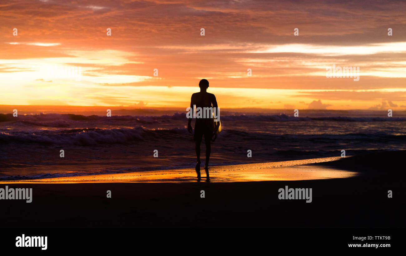 Silhouette de pleine longueur avec touristiques à la planche en mer en se tenant sur le rivage contre le ciel au coucher du soleil Banque D'Images