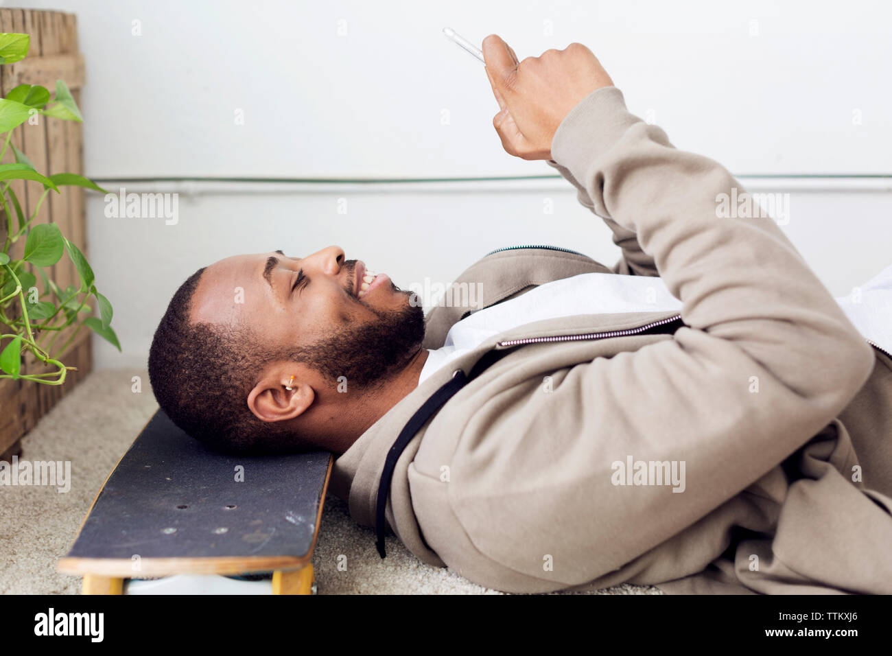 Vue latérale du portrait à l'aide de smart phone while resting head on skateboard à creative office Banque D'Images