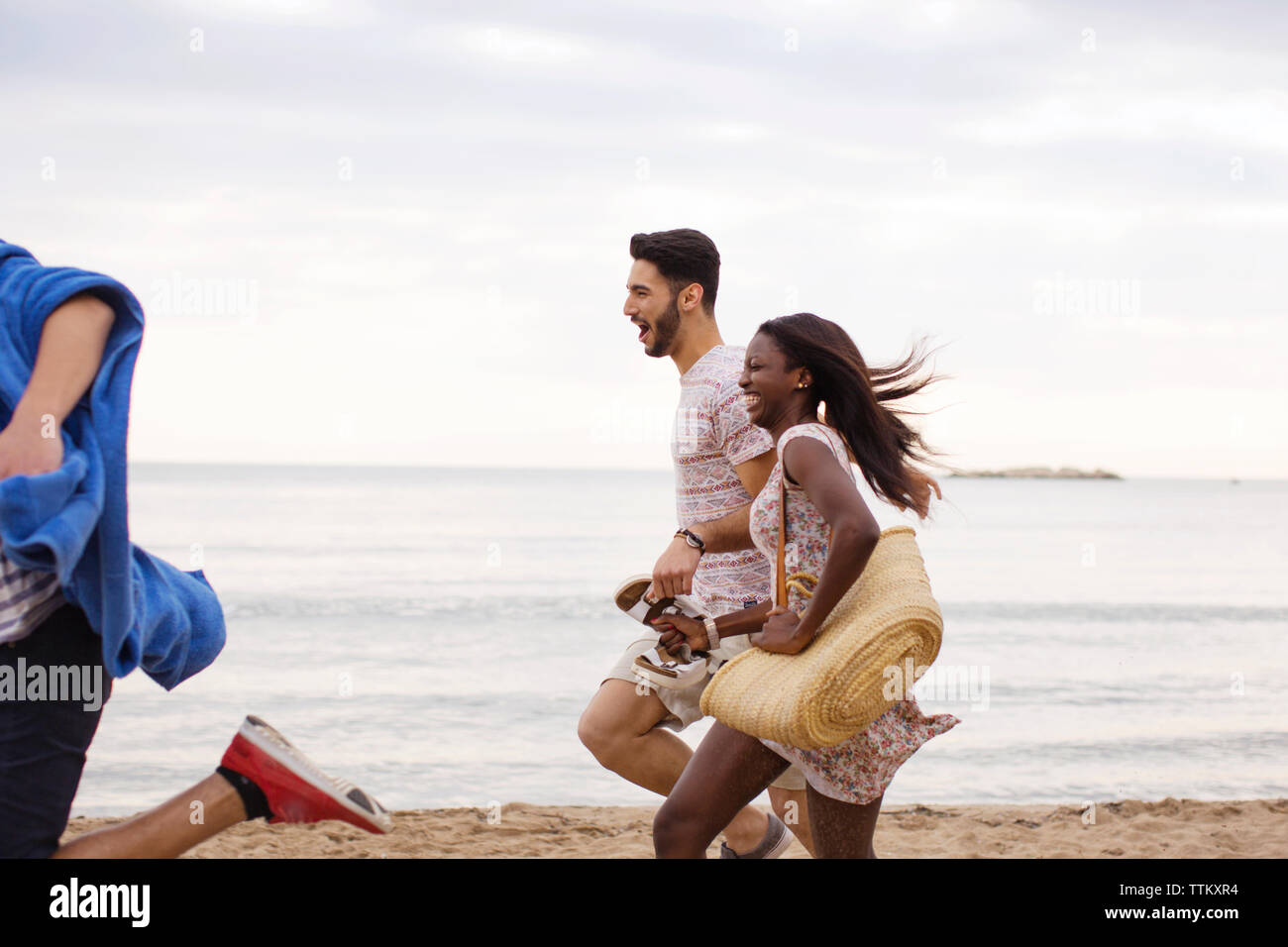 Vue latérale du cheerful multi-ethnic friends running on shore at beach Banque D'Images