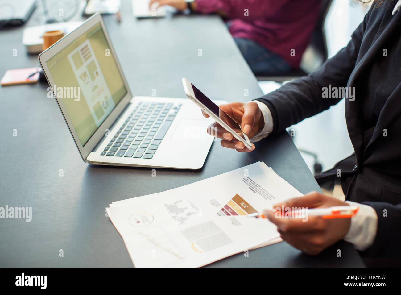 Portrait of businesswoman using mobile phone alors que l'analyse des données dans office Banque D'Images