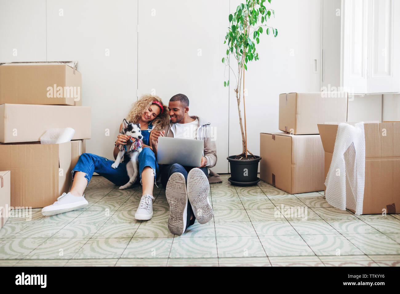 Heureux couple Playing with dog lors de l'utilisation d'un ordinateur portable à l'accueil Banque D'Images