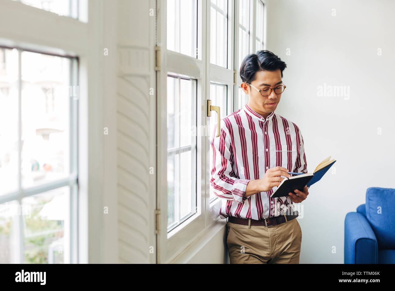 homme d'affaires regardant dans le journal tout en se tenant debout contre les fenêtres dans le bureau Banque D'Images