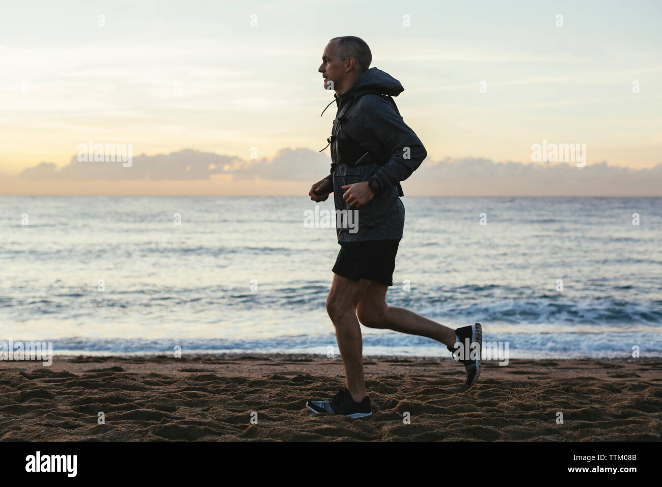 Vue de côté de l'homme de courir contre le ciel au coucher du soleil plage Banque D'Images