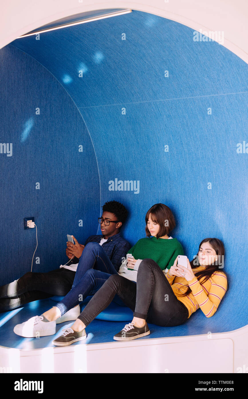 Des amis à l'aide de téléphones intelligents tout en restant assis à bibliothèque Banque D'Images