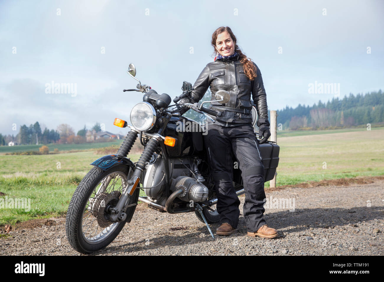 Portrait de femme portant des motards blouson de cuir tout en se tenant en moto sur route de terre Banque D'Images