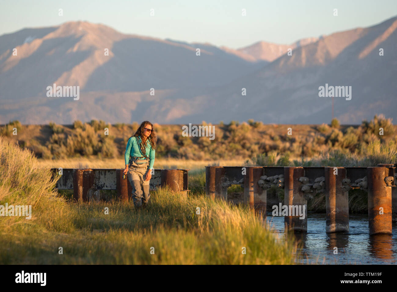 Jeune femme avec la canne à pêche dans la rivière Owens contre montagne Banque D'Images