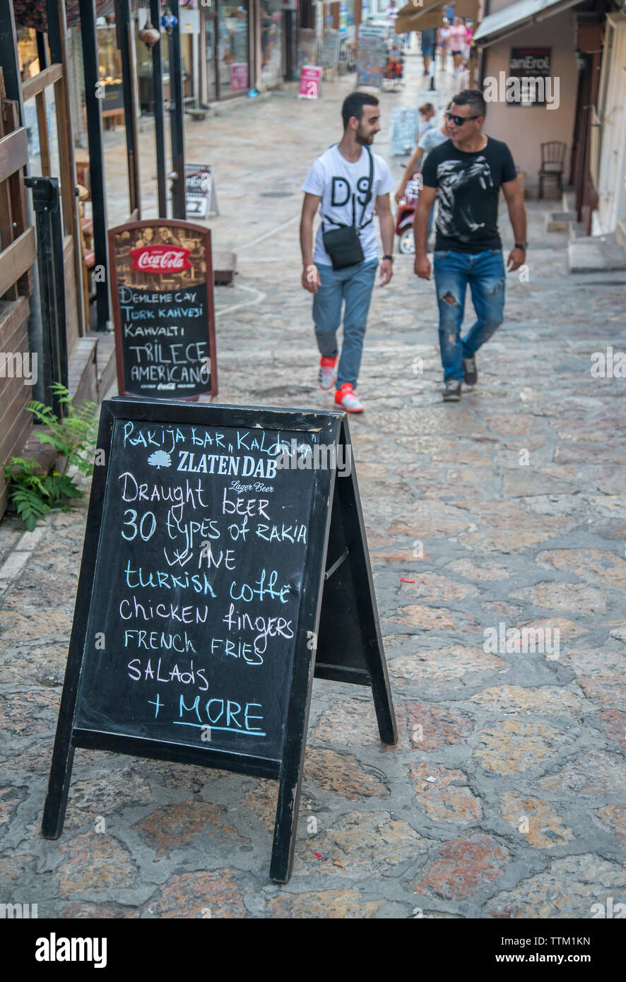 Deux hommes s'approchent d'un conseil de la chaussée à l'extérieur d'un bar/restaurant de la nourriture et des boissons, de la publicité sur une rue étroite dans la zone vieux bazar de Skopje. Banque D'Images