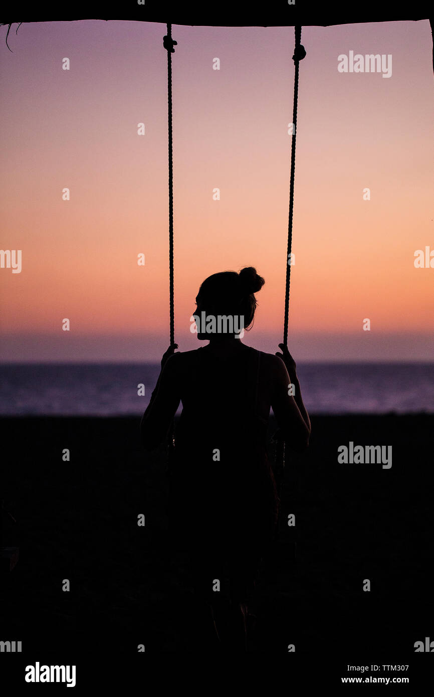 Vue arrière de silhouette femme balançant à la sky pendant le coucher du soleil Banque D'Images