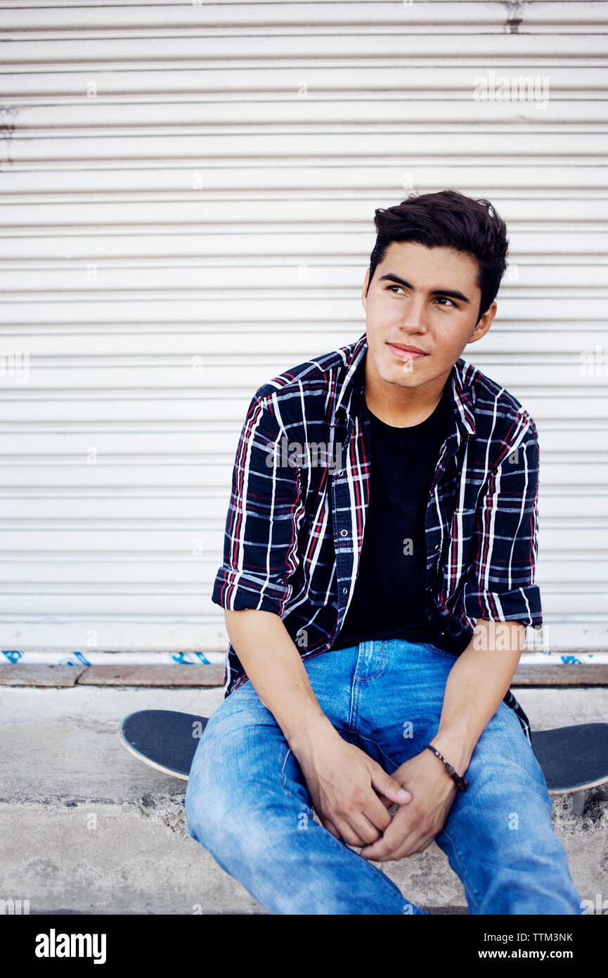 Smiling man sitting on skateboard assis contre l'obturateur fermé Banque D'Images
