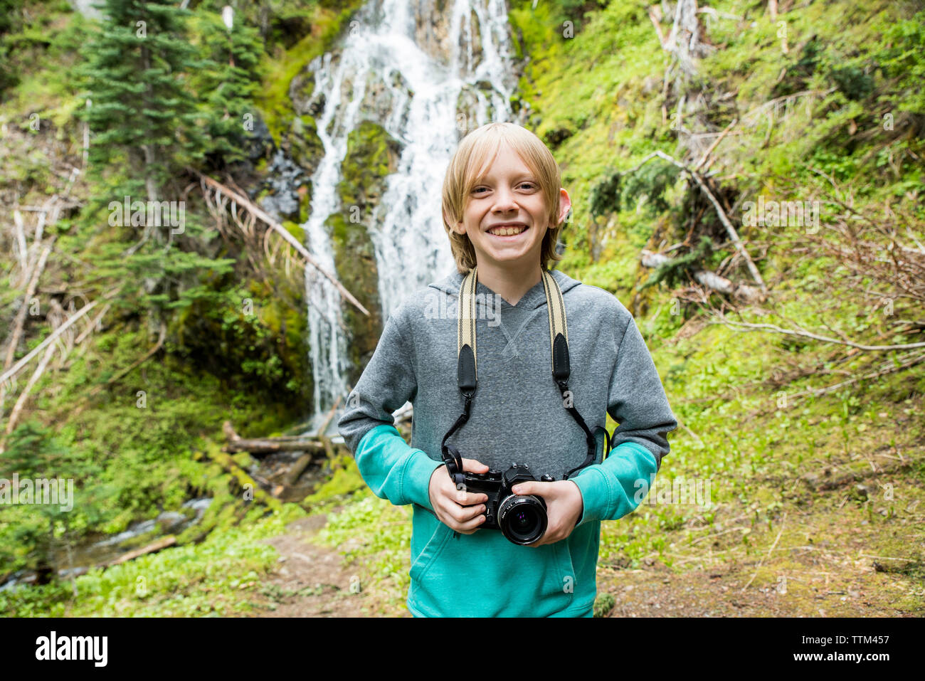 Portrait of smiling boy holding camera debout contre la cascade dans le Parc National Olympique Banque D'Images