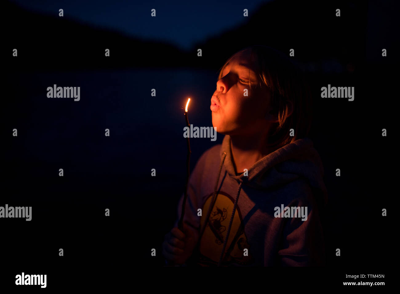 Boy blowing burning stick tout en se tenant dans le Parc National Olympique de nuit Banque D'Images