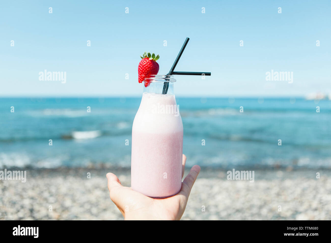 Cropped hand of man holding jus de fraises en bouteille at beach Banque D'Images