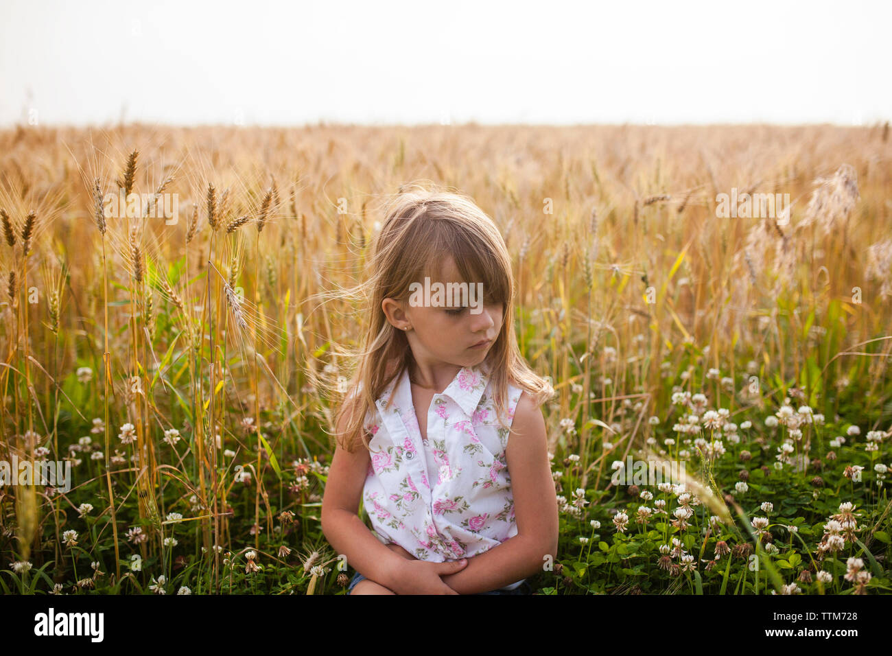 Upset girl sitting on field against sky in farm Banque D'Images